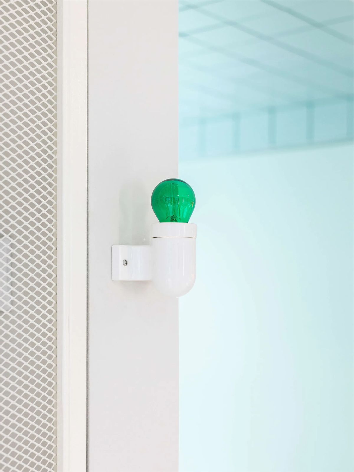 Green glass bulb on a white porcelain wall lamp beside a mint-tinted frosted glass wall