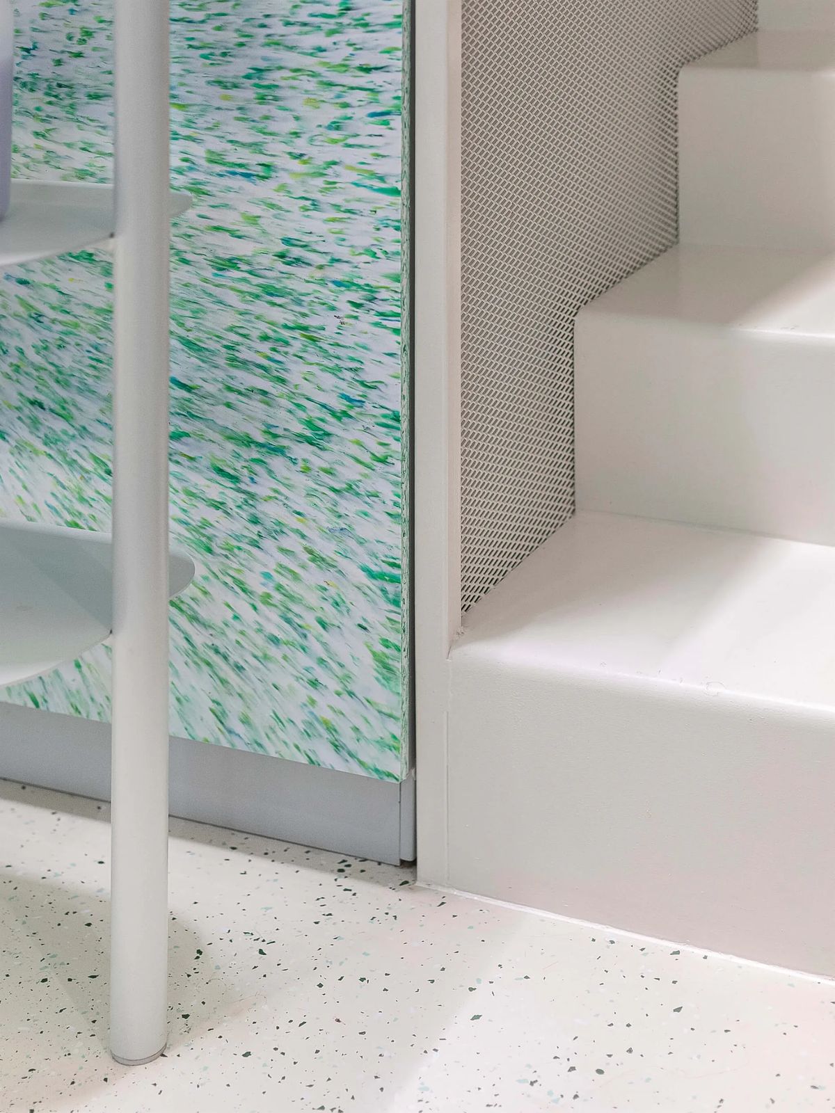 Detail of white stair treads meeting a green speckled panel and a terrazzo floor