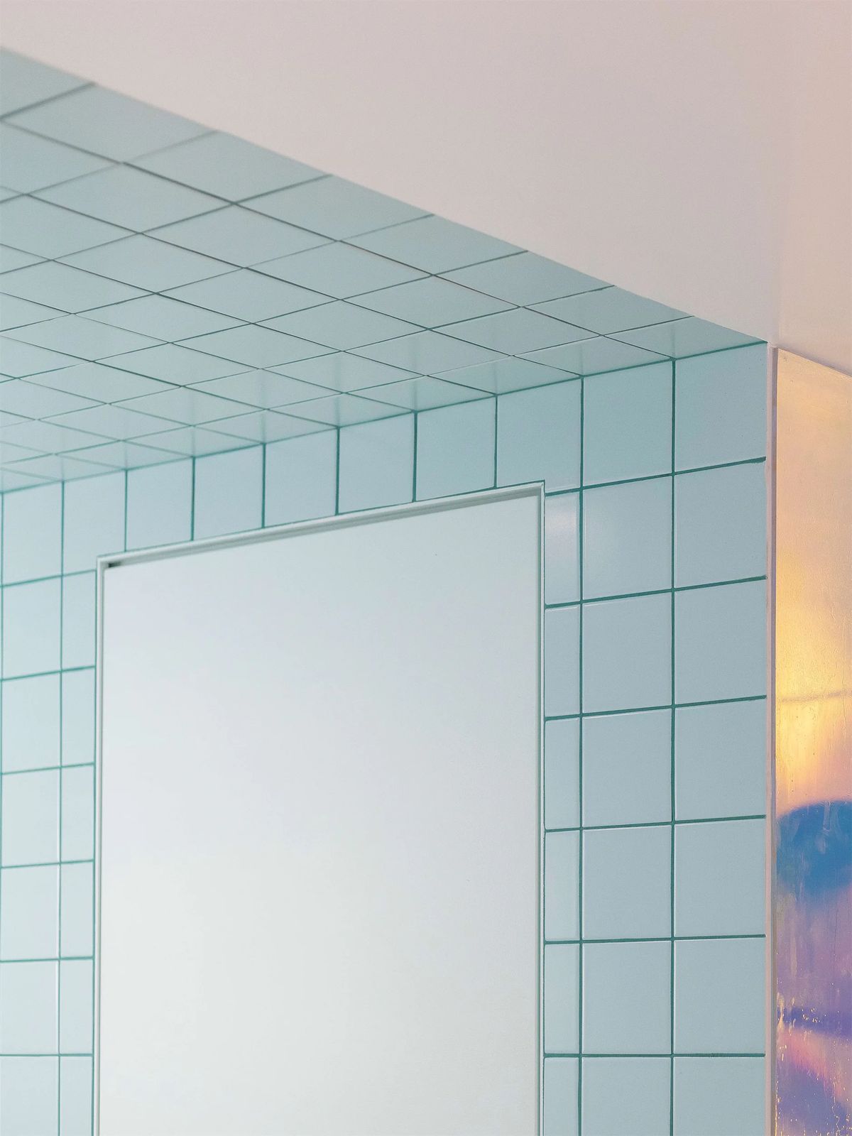 Rectangular mirror set into mint tiles with dark grout that wrap up onto the ceiling