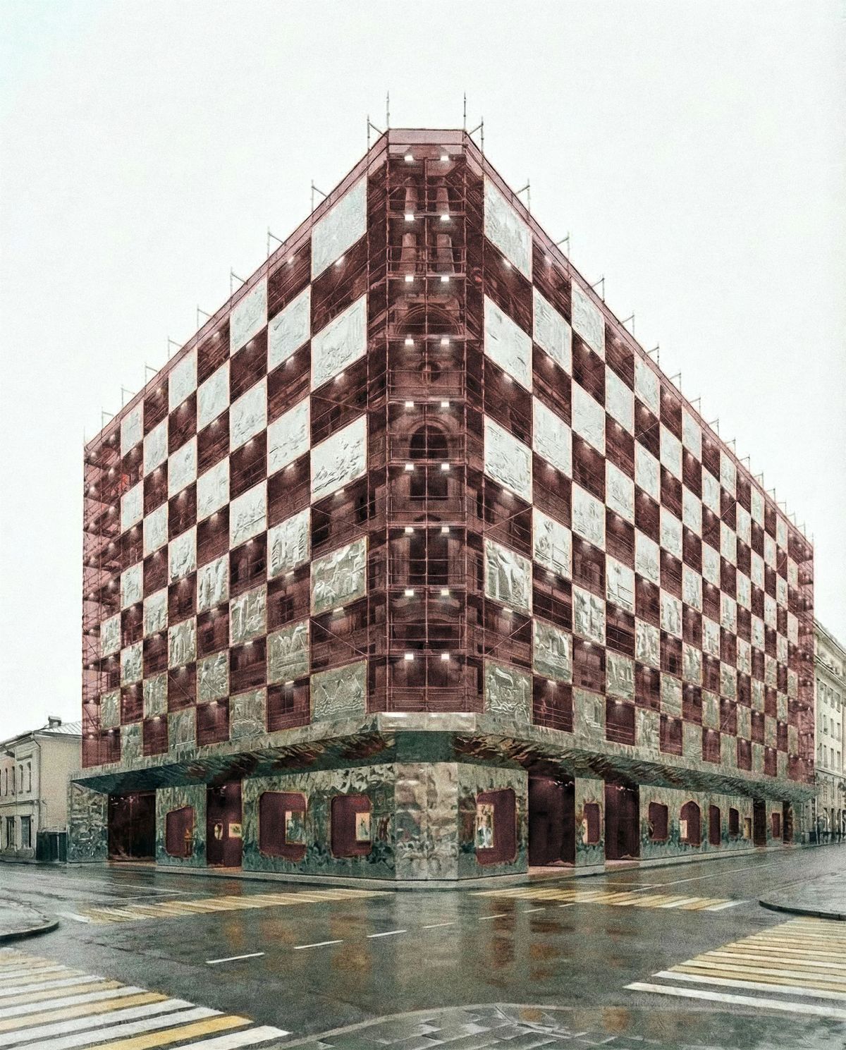 Corner building wrapped in red scaffolding with a checkerboard of silver relief panels on a rainy street