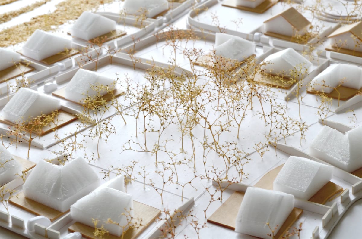 Detail of the model with white gabled houses on wooden plots among delicate dried-plant trees