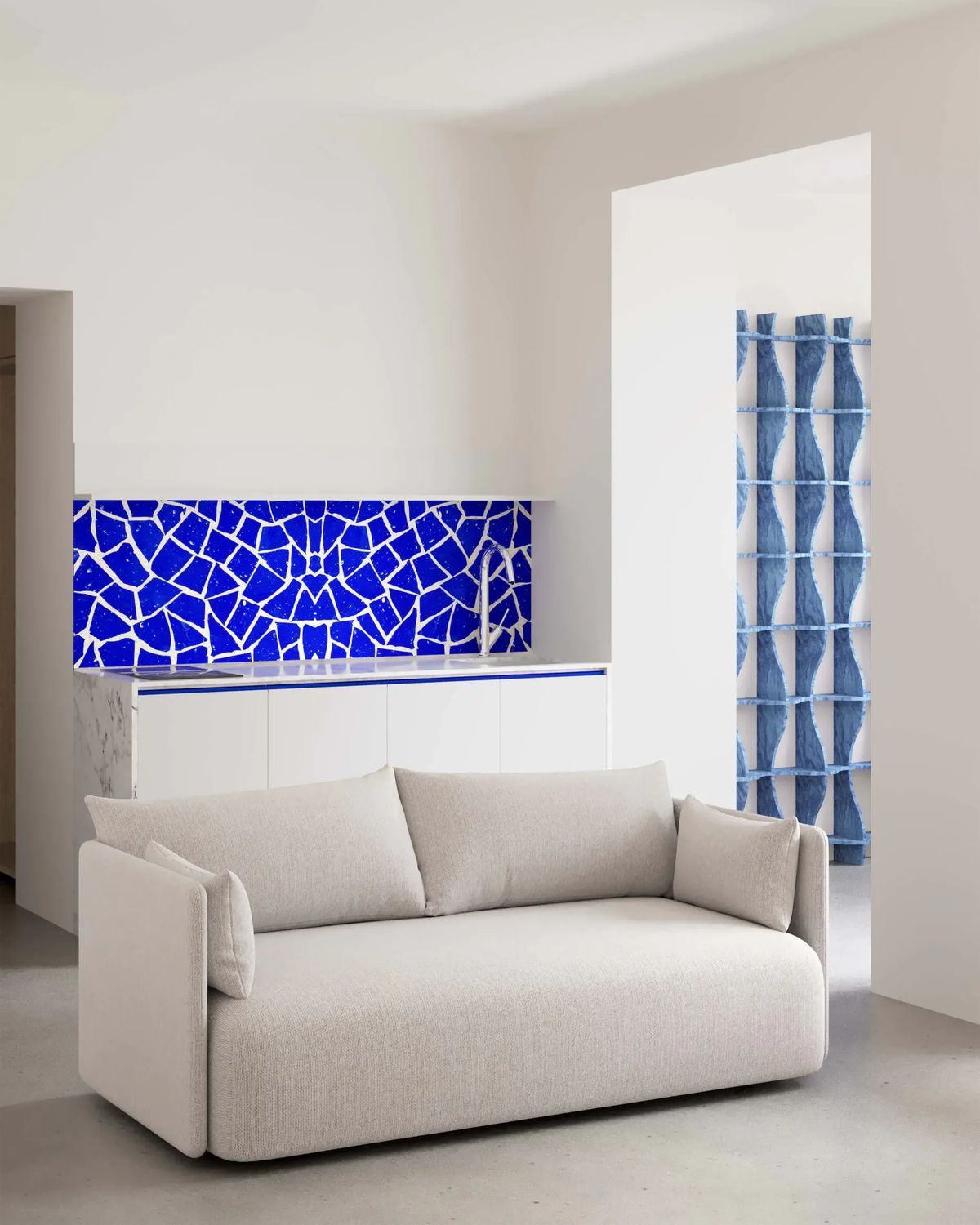 Pale bouclé sofa before a kitchenette with a cobalt blue broken-tile backsplash and a blue sculptural shelf