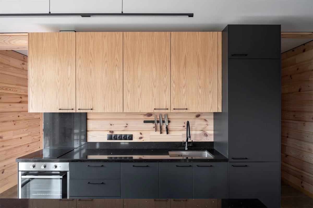 Front view of a kitchen with light wood upper cabinets, dark lower units and a tall graphite column