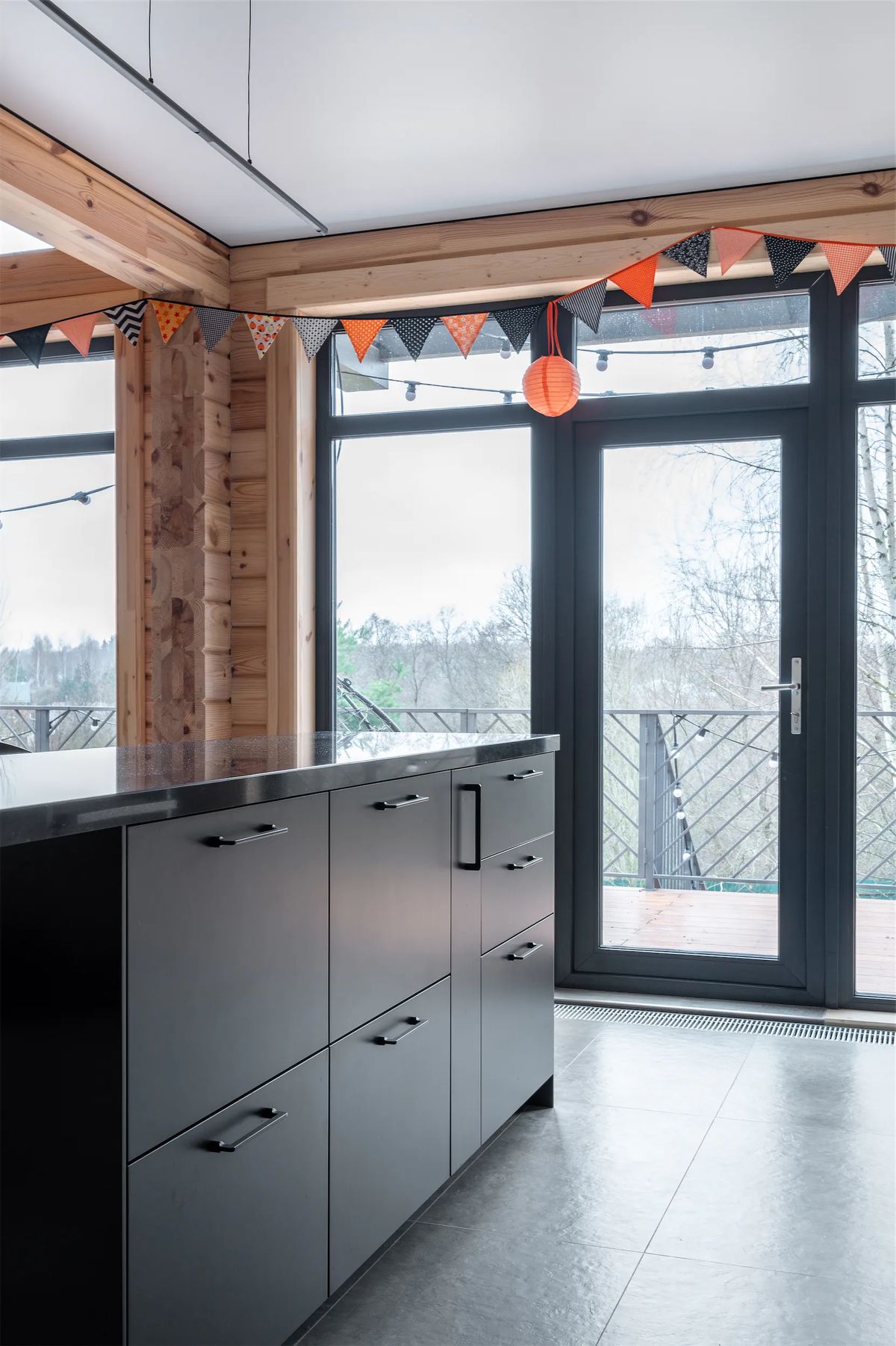Dark kitchen island beside floor-to-ceiling windows and a glazed door to a balcony with bunting