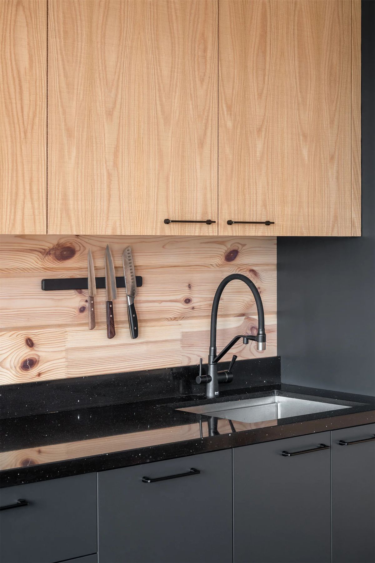 Black mixer tap and steel sink set in a sparkling black worktop below light wood cabinets