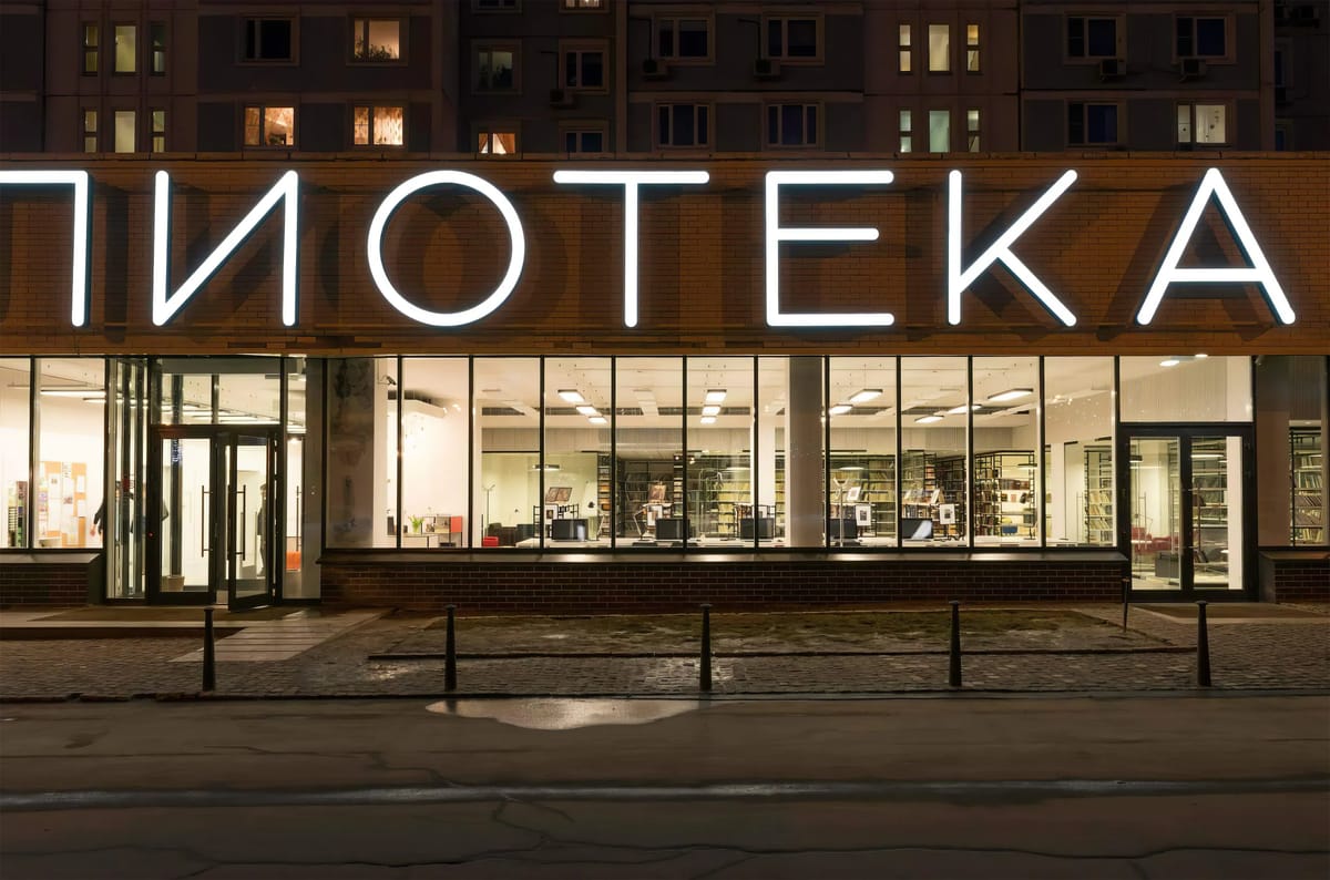 Library at night with large illuminated letters over a glazed brick ground floor beneath apartment towers