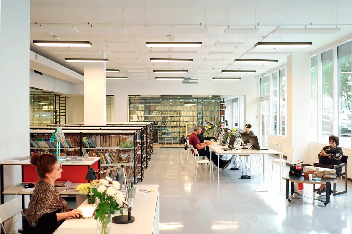 Bright reading room with white tables, linear ceiling lights, low bookshelves and tall windows