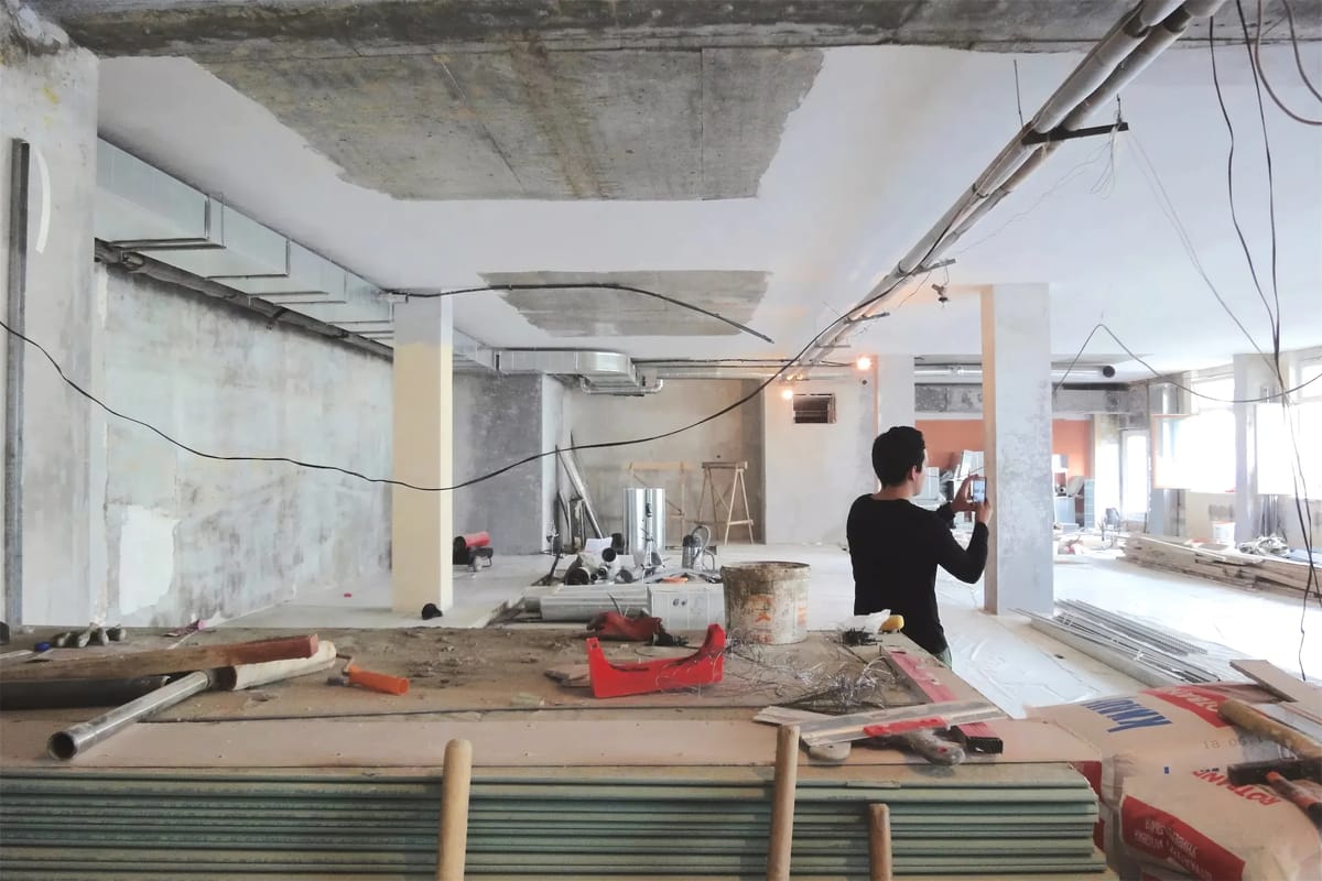 Construction site with bare concrete, exposed cables, tools and plasterboard as a person photographs the space