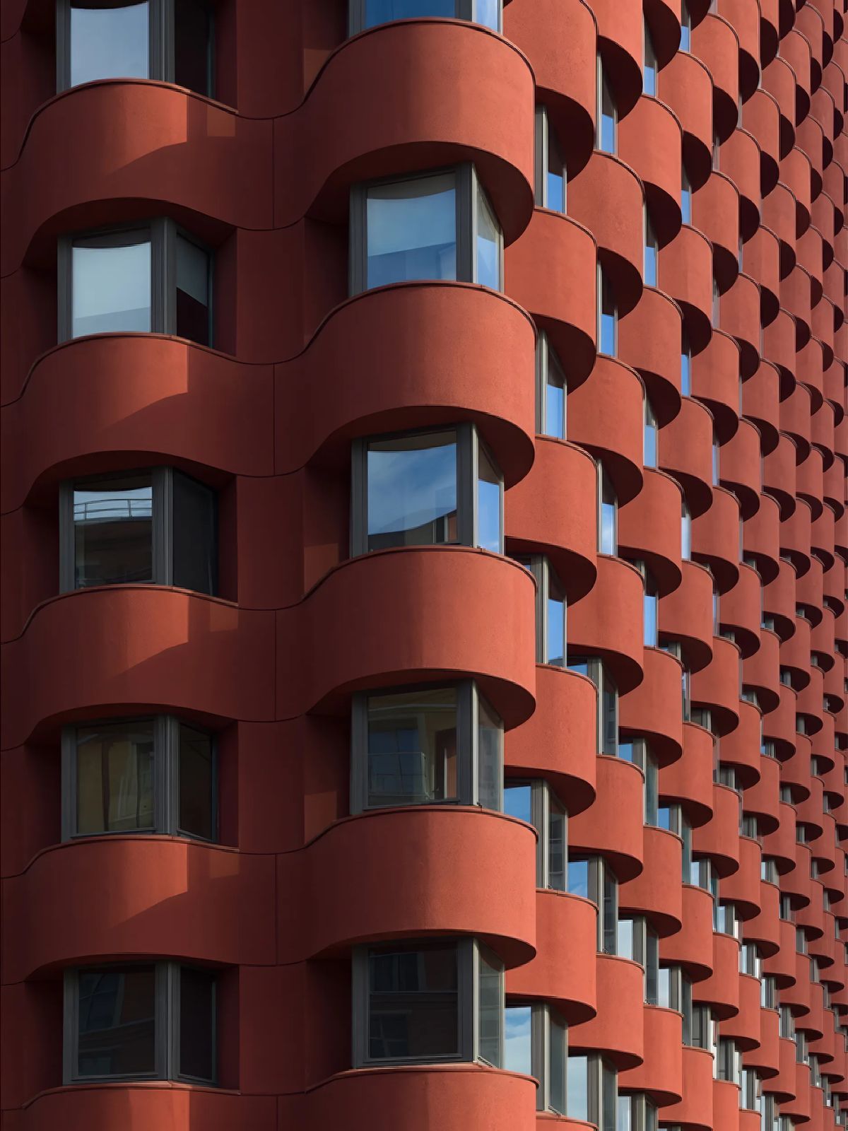 Rhythmic red facade of rounded window bays receding in perspective, catching low sunlight