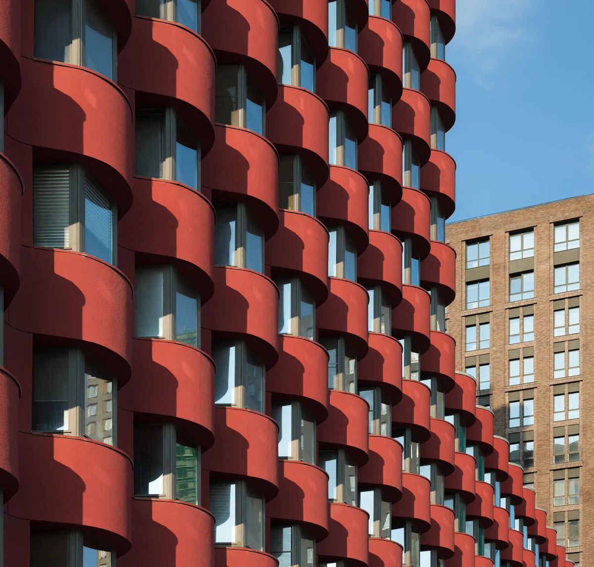 Undulating red bay windows casting deep shadows, with a brick housing block behind
